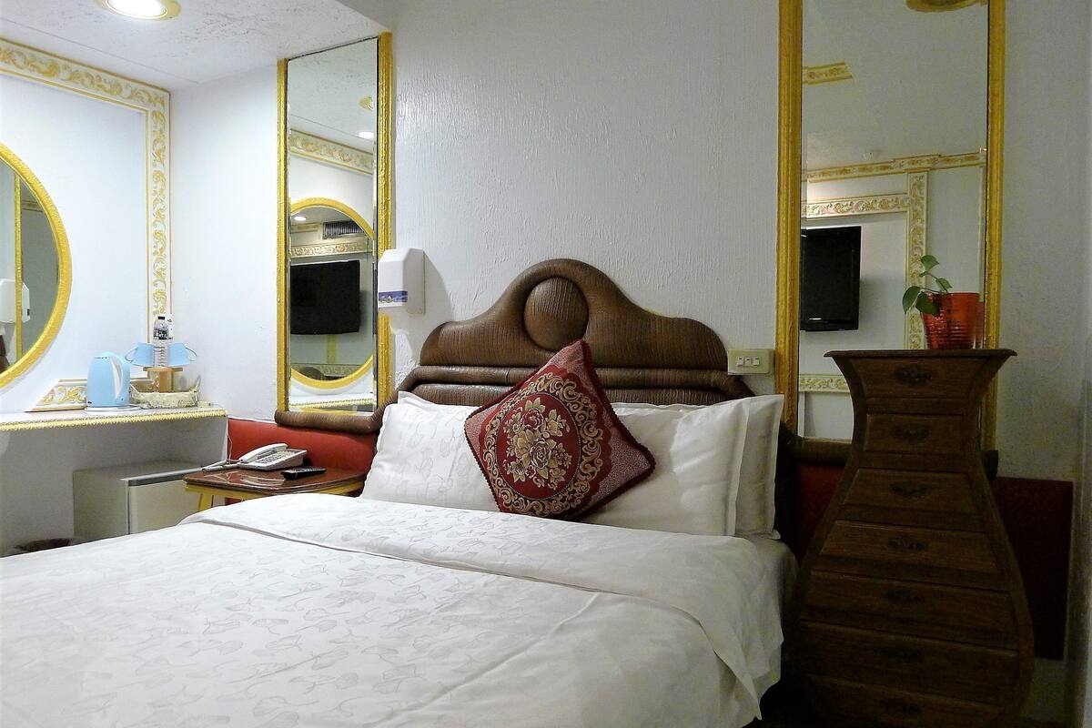 Habitación de hotel con una cama grande, un tocador de madera, un espejo, un escritorio con lámpara y un televisor.