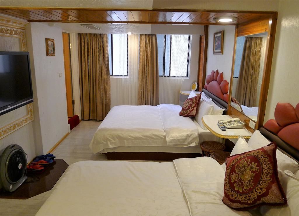 Habitación de hotel con dos camas, televisión, mesita de noche con teléfono y espejo.