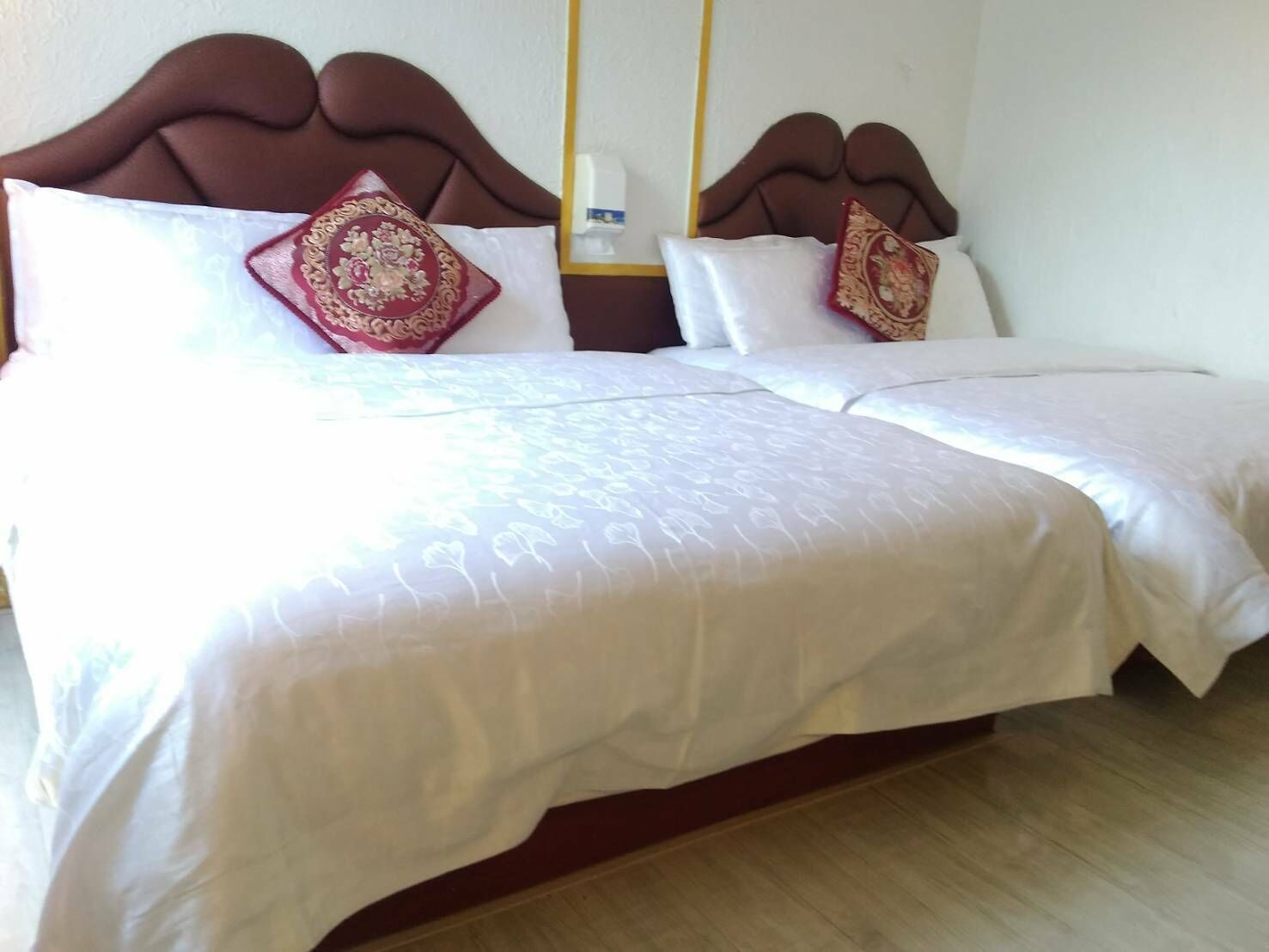 A double bed with white linens and decorative pillows, a wooden headboard, and a bedside table with a lamp.