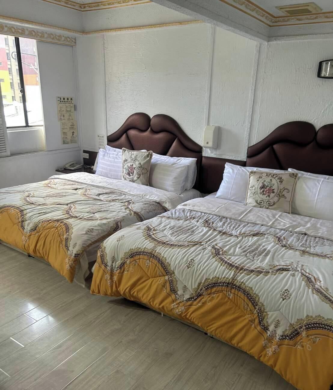 Habitación de hotel con dos camas, una ventana y un aplique de pared.