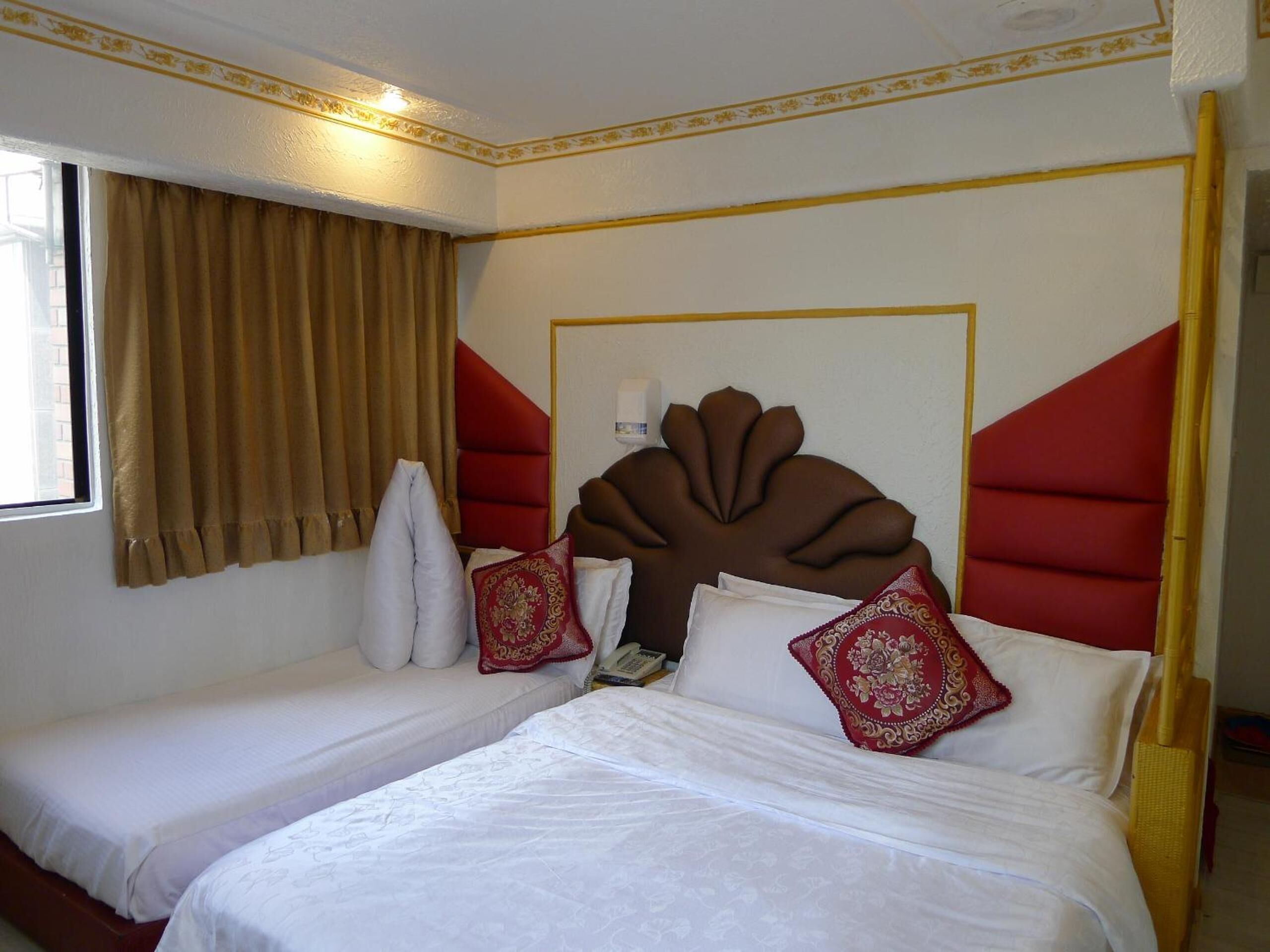 A hotel room with two beds, a large decorative headboard, and a window with curtains.