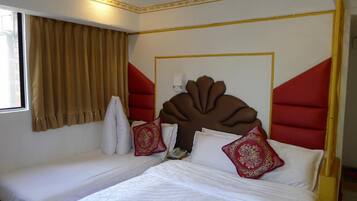 A hotel room with two beds, a large decorative headboard, and a window with curtains.