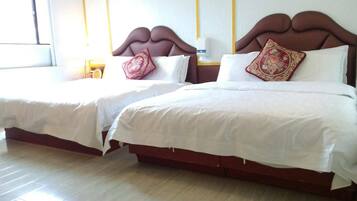 Dos camas dobles con sábanas blancas y almohadas decorativas, suelo de madera y una ventana con cortinas.