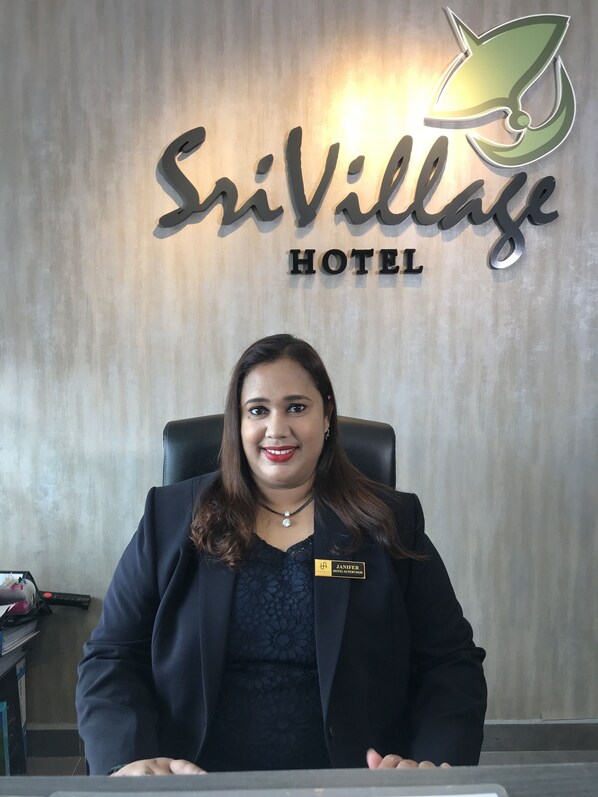 Zona de recepción de un hotel con un cartel que dice 'SriVillage Hotel' y un logotipo.