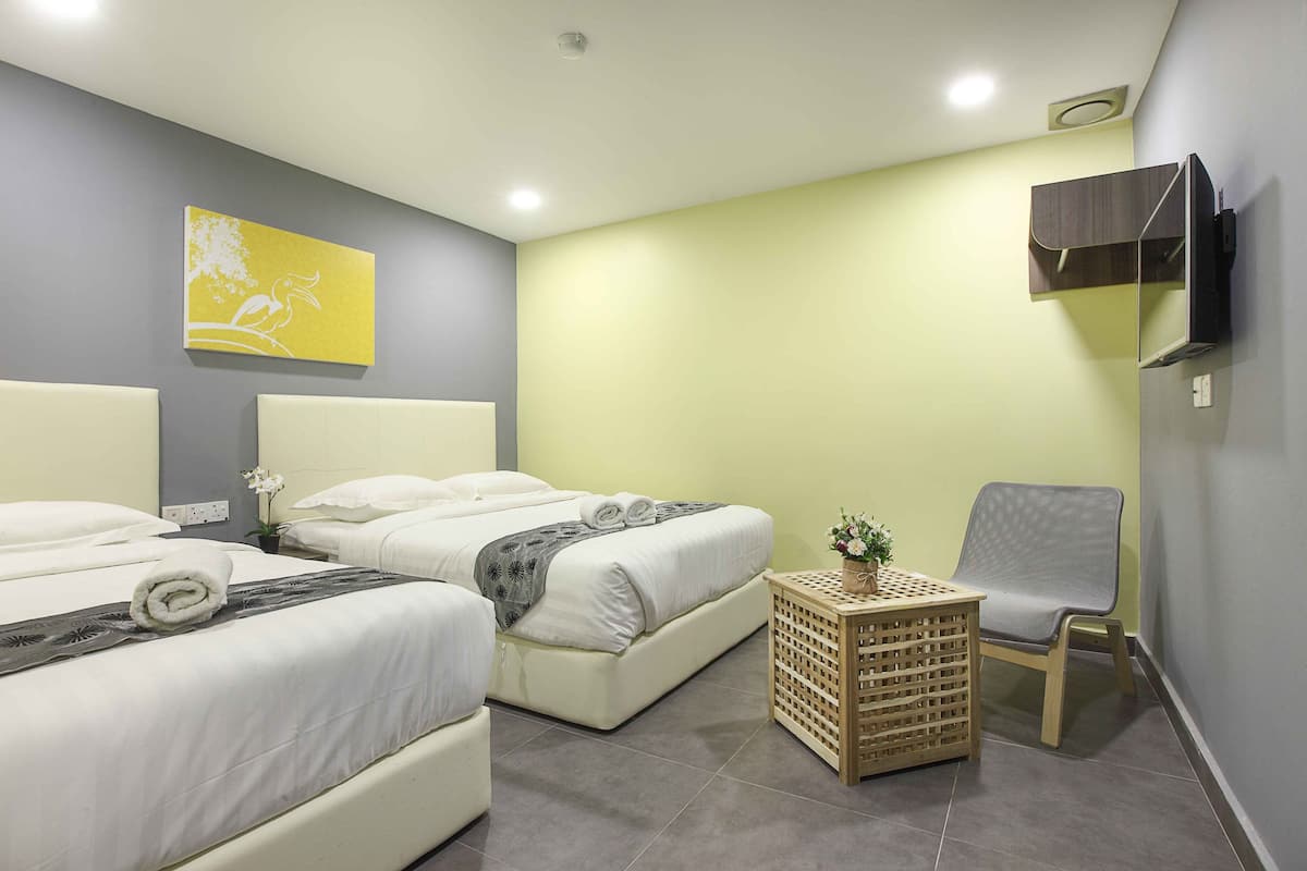 Quarto de hotel com duas camas, uma mesinha com uma planta, uma cadeira e uma televisão na parede.