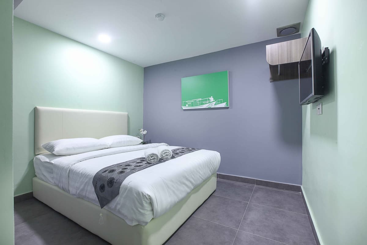 Quarto de hotel com uma cama, uma TV montada e uma obra de arte verde na parede.