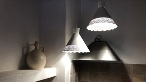 A bathroom with a tiled wall, a shelf with a vase, and two pendant lights with lace shades.