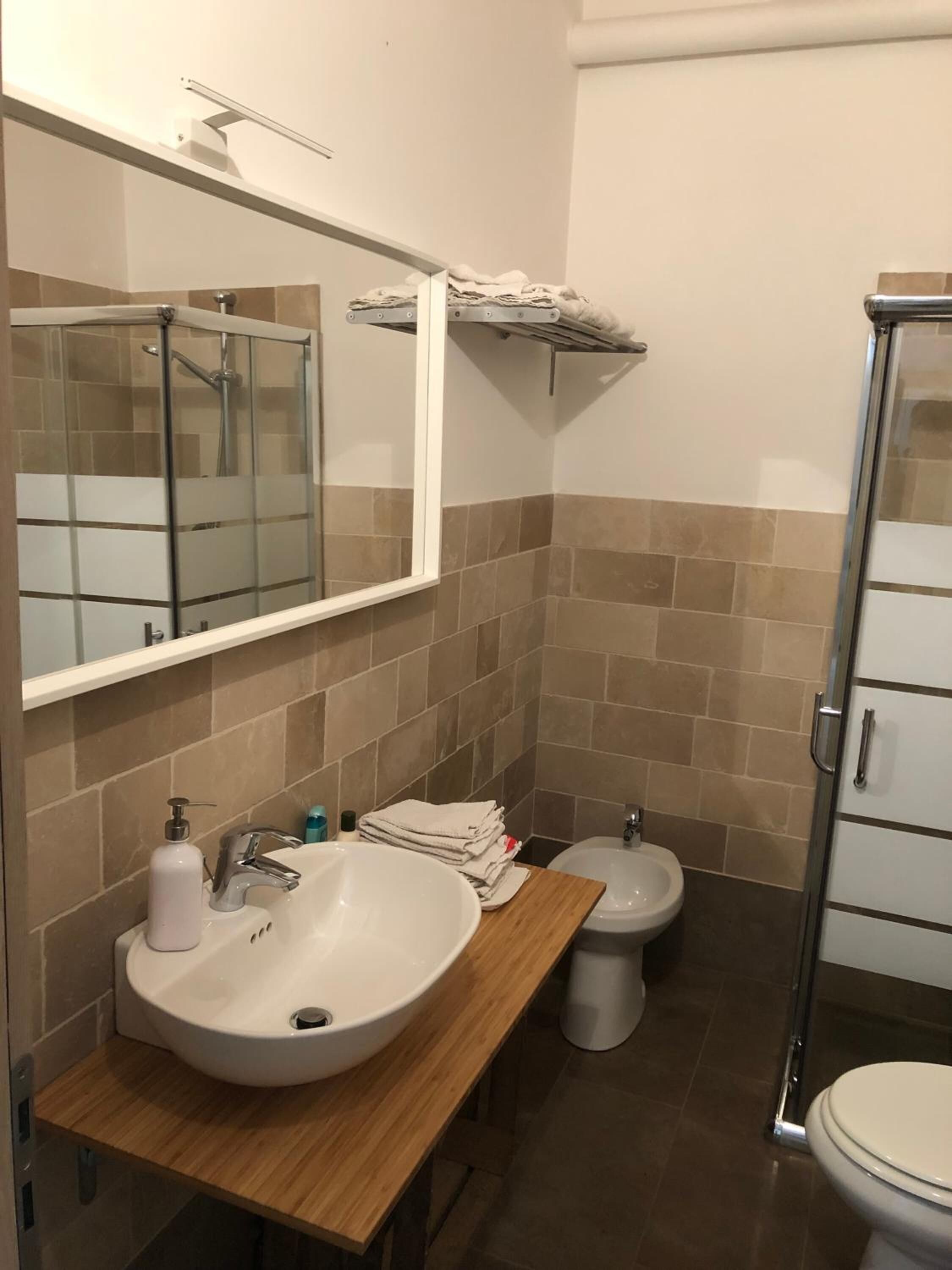A bathroom with a large sink, a mirror, a shower enclosure, and a toilet.
