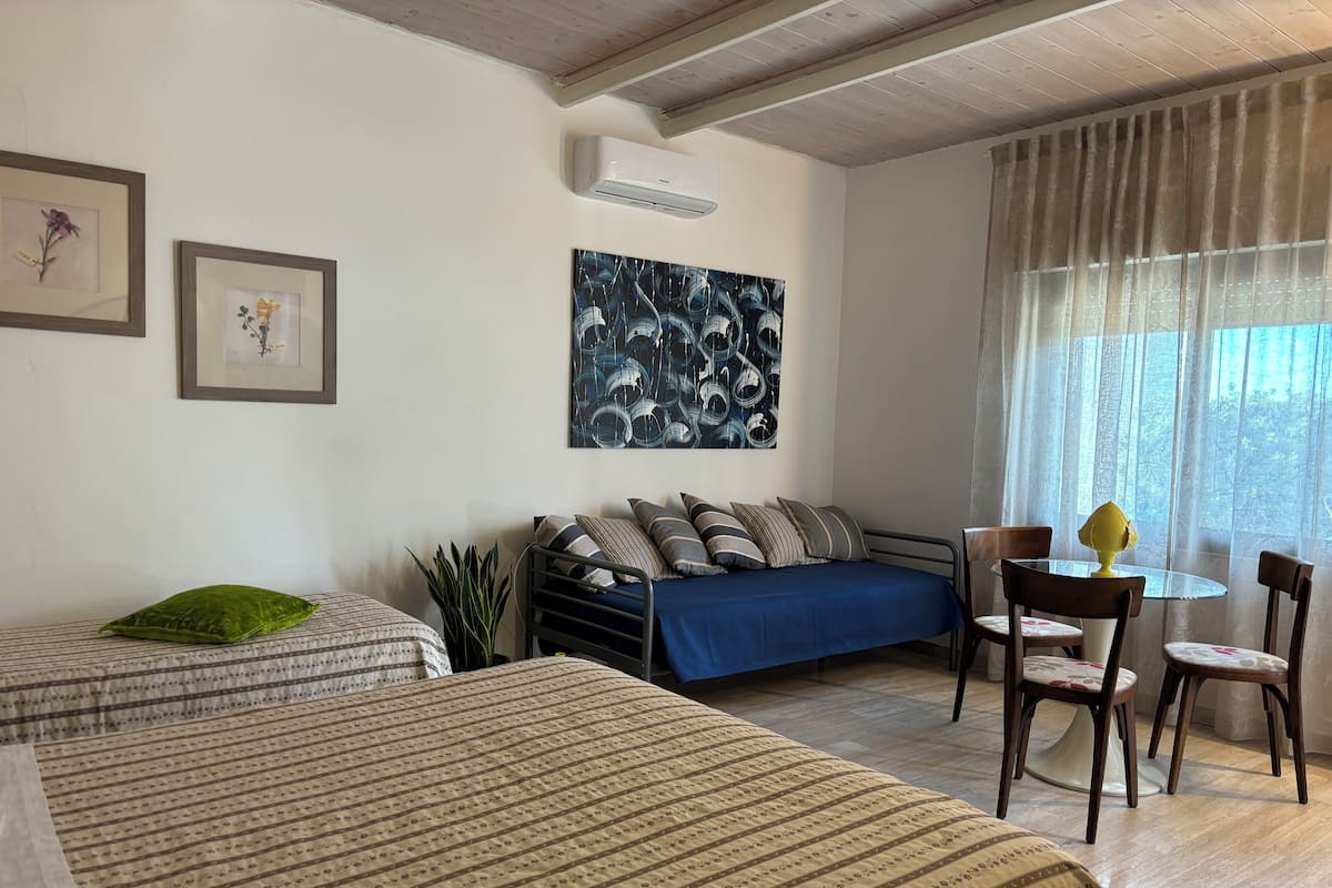 Un dormitorio con dos camas, un sofá, una mesa de comedor con sillas y un cuadro abstracto grande en la pared.