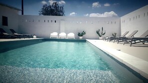 Una piscina rectangular con agua cristalina, rodeada de muros blancos y algunas plantas en macetas.