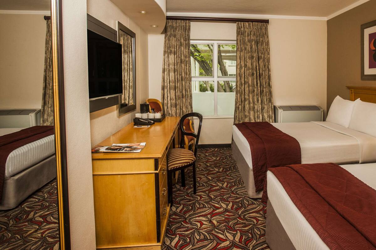 Een hotelkamer met een bed, een bureau, een stoel, een televisie en een raam met gordijnen.