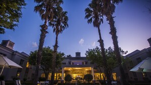 A poolside view of a hotel with palm trees, lounge chairs, and a well-lit entrance.