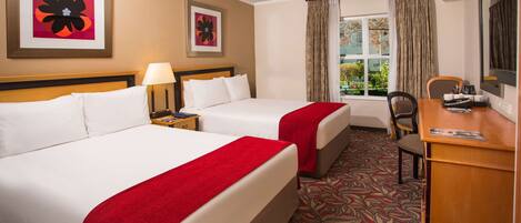 A hotel room with two beds, a desk, a chair, and a window with curtains.