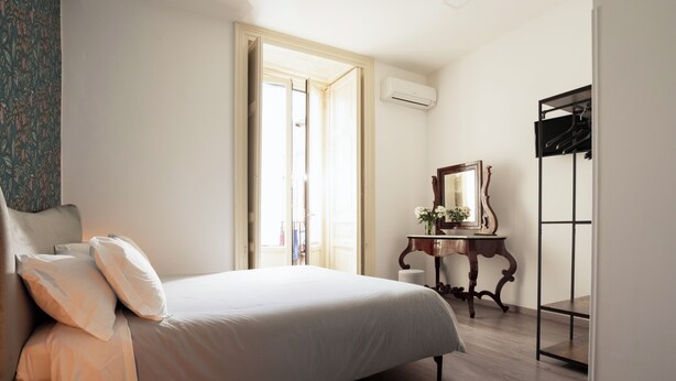 A bedroom with a bed, a dresser, a mirror, and an open door leading to another room. - B&B Università (Catania)