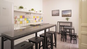 A kitchen with a long countertop, bar stools, a white refrigerator, and a colorful backsplash. - B&B Università (Catania)