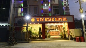 Een hotel met een opvallend bord waarop 'WIN STAR HOTEL' staat. Het heeft meerdere verdiepingen met balkons, en de ingang is verlicht.