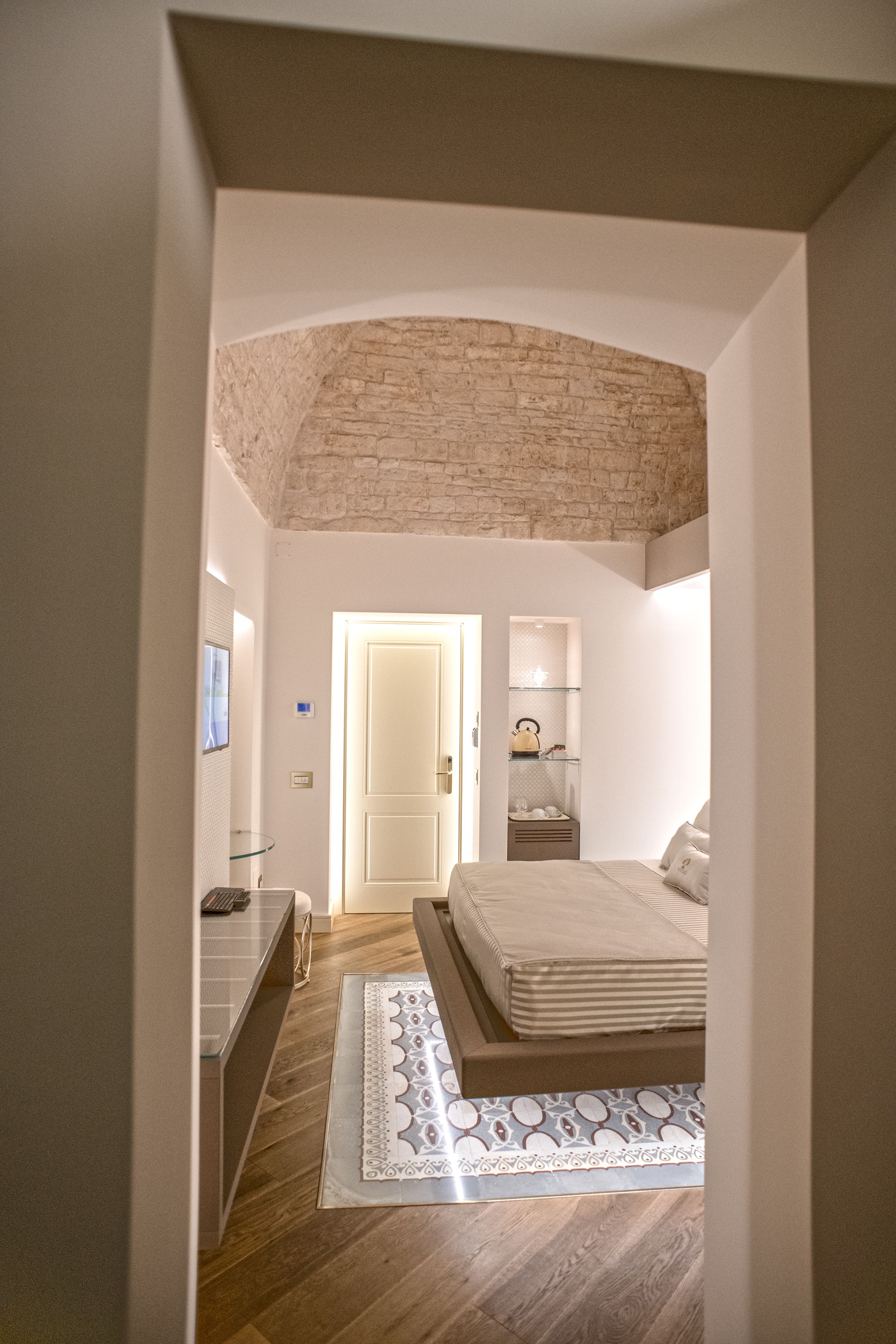 A bedroom with a wooden floor, a bed with a white mattress, a bedside table, and a nightstand.