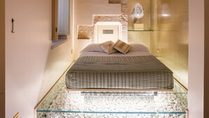 A bedroom with a bed, a glass coffee table, and a stone wall. - Palazzo Scotto (Alberobello)