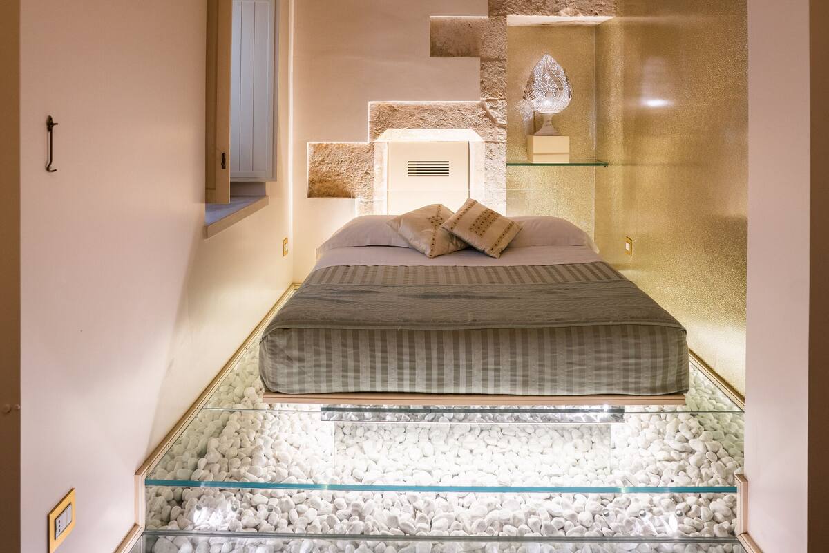 Une chambre à coucher avec un lit, une table basse en verre et un mur en pierre.