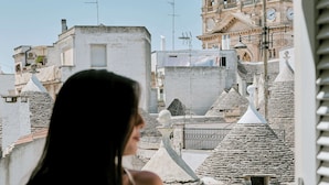 A person overlooking a historic town with terracotta-roofed buildings and a prominent church tower. - Palazzo Scotto (Alberobello)