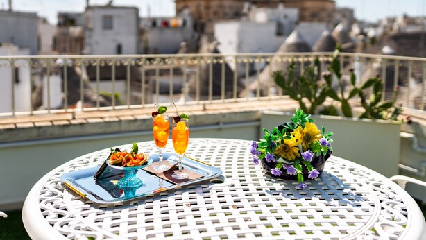 A table with a tray of food and drinks, a vase of flowers, and a cityscape view. - Palazzo Scotto (Alberobello)