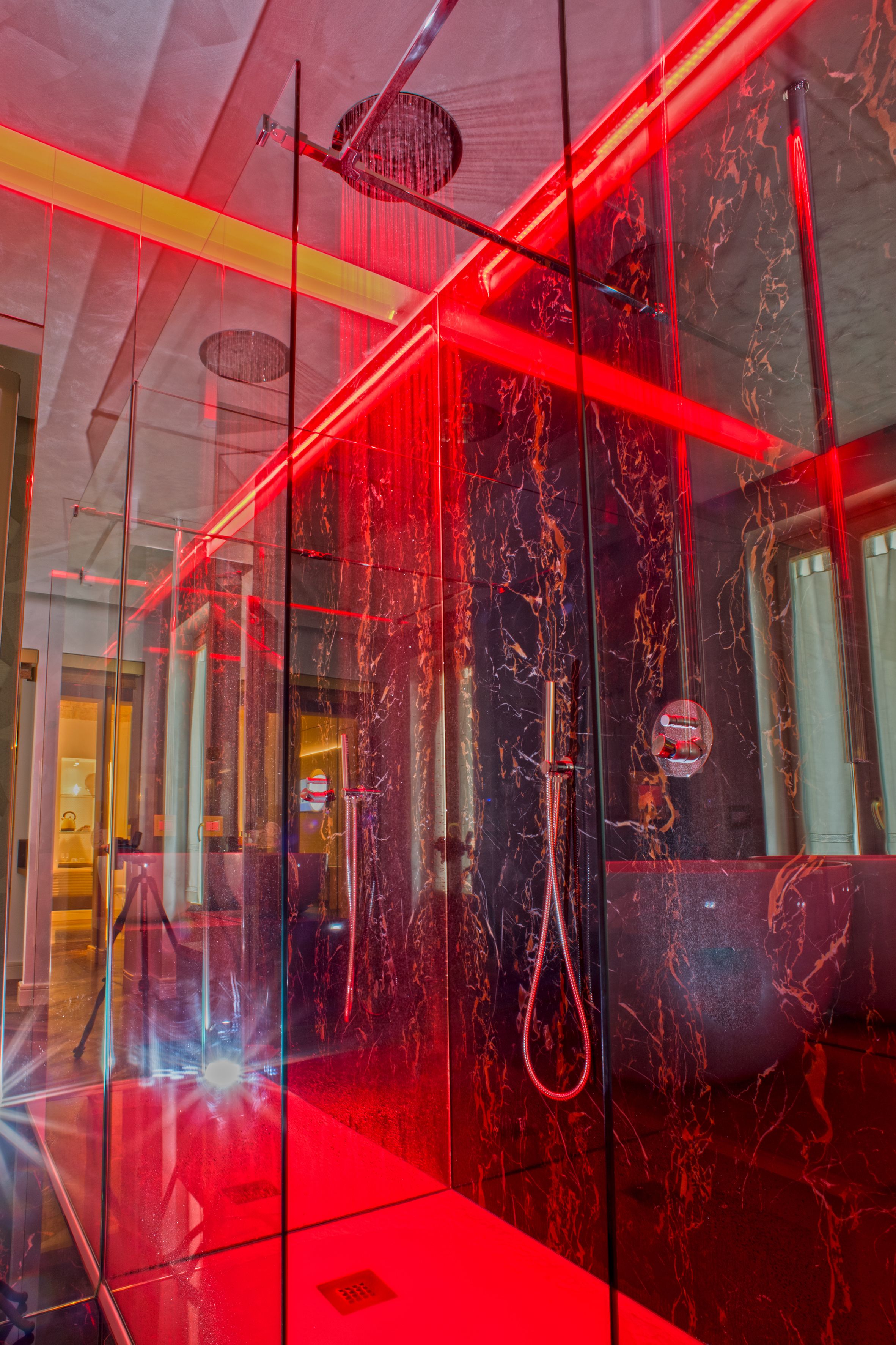 A modern interior with reflective glass walls, a red-lit ceiling, and a visible water feature.