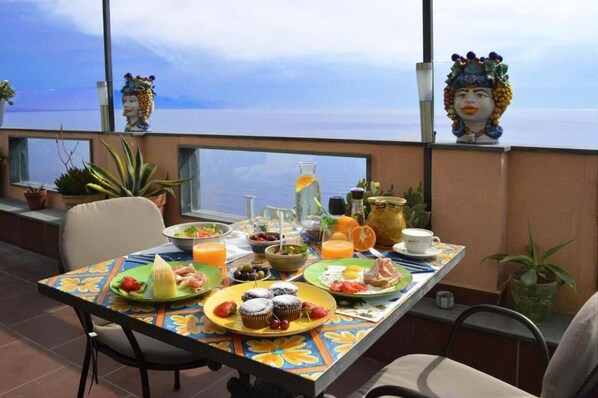 A dining table with breakfast items, potted plants, and decorative items on a balcony overlooking a body of water. - Mar Dei Poeti (Riposto)