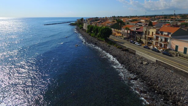 Un pueblo costero con un litoral rocoso, una carretera paralela al mar y edificios con tejados de tejas rojas.