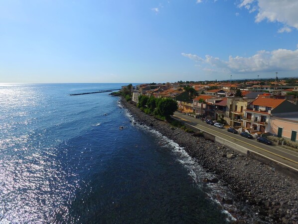Un pueblo costero con un litoral rocoso, una carretera paralela al mar y edificios con tejados de tejas rojas.