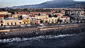 A coastal town with buildings along the waterfront, a road in the foreground, and mountains in the background.
