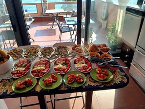 A dining table with various dishes, a view of the sea, and a kitchen area. - Mar Dei Poeti (Riposto)