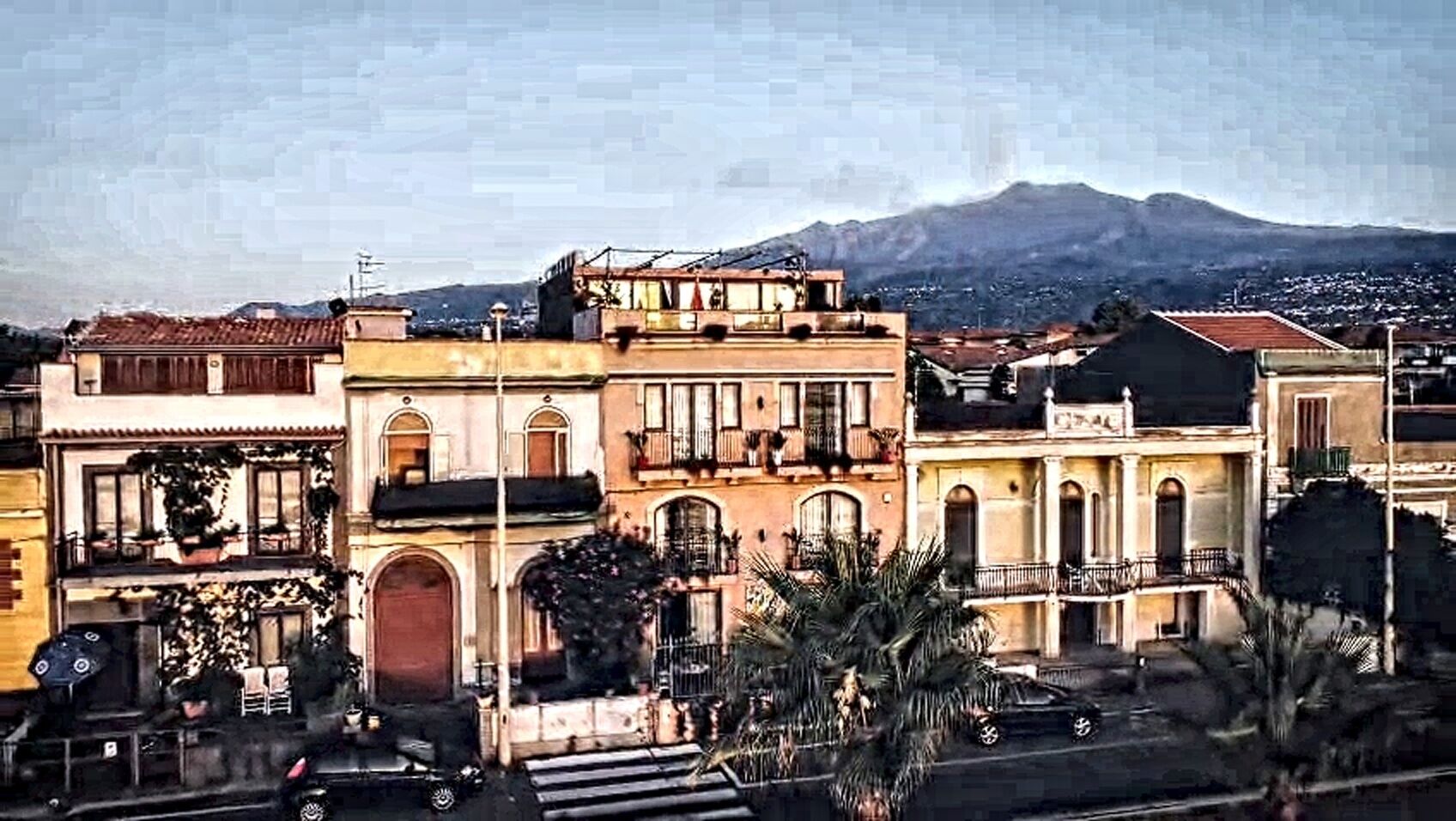 A row of traditional buildings with balconies, a street in front, and a mountain in the background.