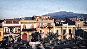 A row of traditional buildings with balconies, a street in front, and a mountain in the background. - Mar Dei Poeti (Riposto)