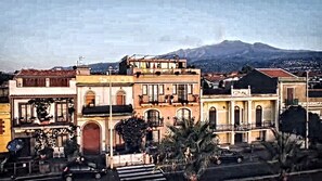 Una hilera de edificios tradicionales con balcones, una calle al frente y una montaña al fondo.