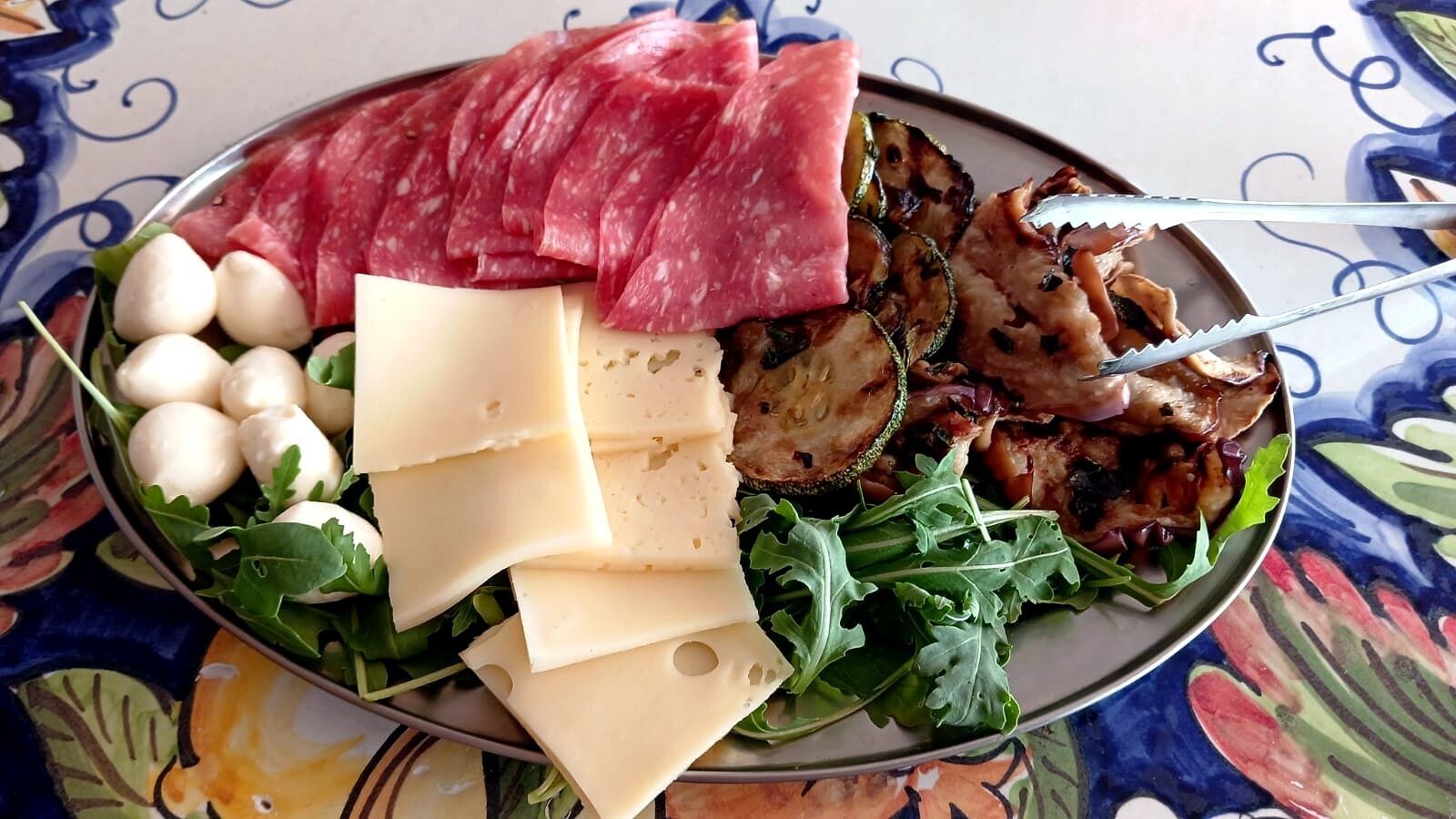 Ein Teller mit verschiedenen Speisen, darunter Fleischscheiben, Käse und Gemüse.