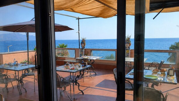 Un espace extérieur aménagé pour les repas, avec des tables et des chaises, donnant sur une étendue d’eau.