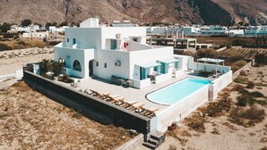 A white building with a pool, surrounded by dry grass and mountains. - Daylight (Santorini)