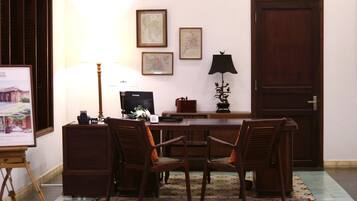 A room with a wooden desk, two chairs, a lamp, framed pictures on the wall, and a door.
