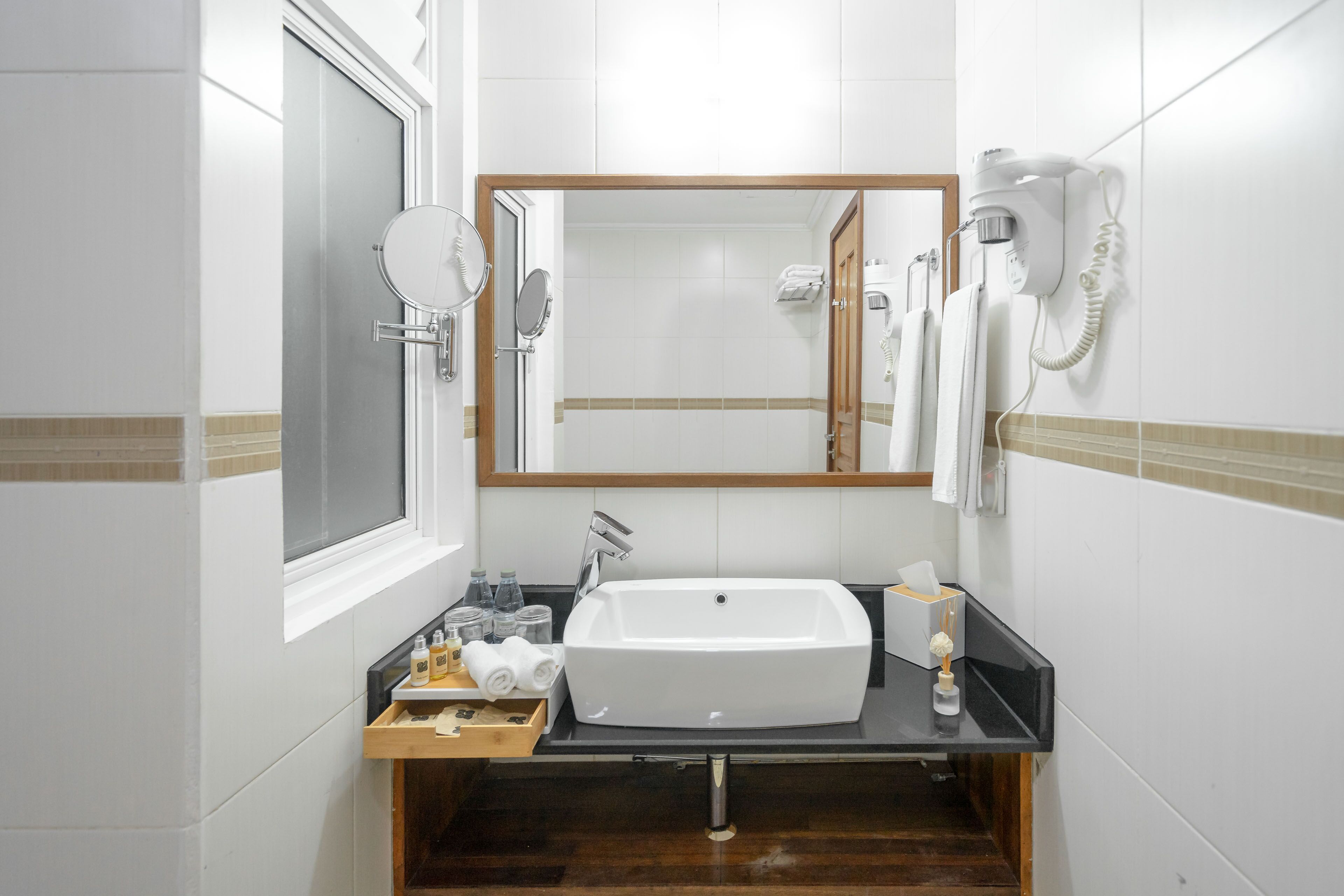 Un baño con lavamanos blanco, espejo, secador de pelo y toallero.