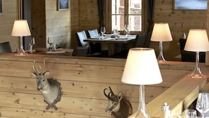 Un interno in legno con tavoli apparecchiati per la cena, illuminato da lampade e bicchieri di vino.