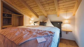 A bedroom with a wooden ceiling, a bed with a brown blanket, a nightstand with a lamp, and a wooden wardrobe.