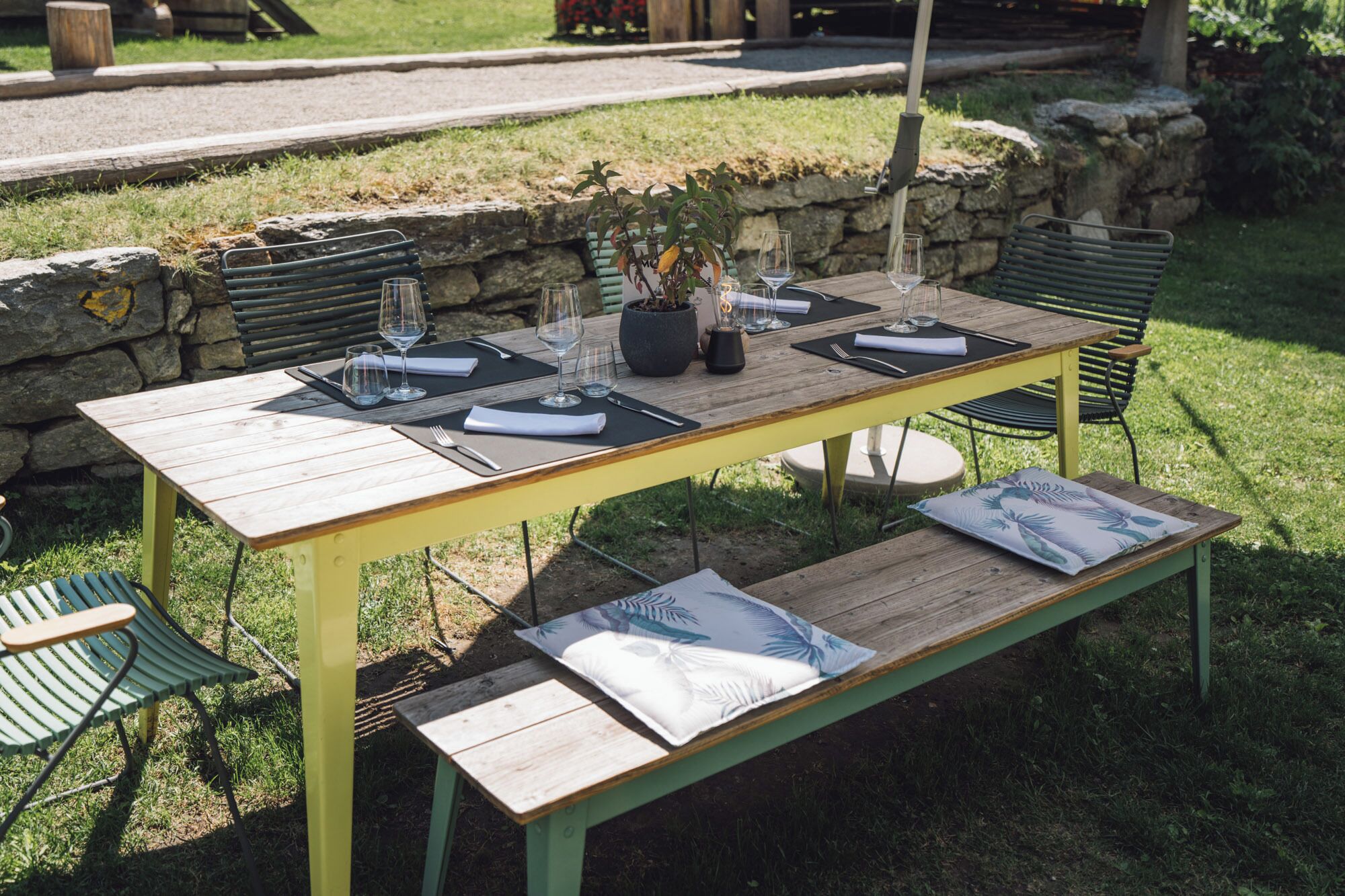 An outdoor dining area with a wooden table set for four, surrounded by chairs and a bench.