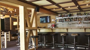 Angolo bar con travi in legno, una TV a parete e diverse bottiglie e bicchieri sugli scaffali.