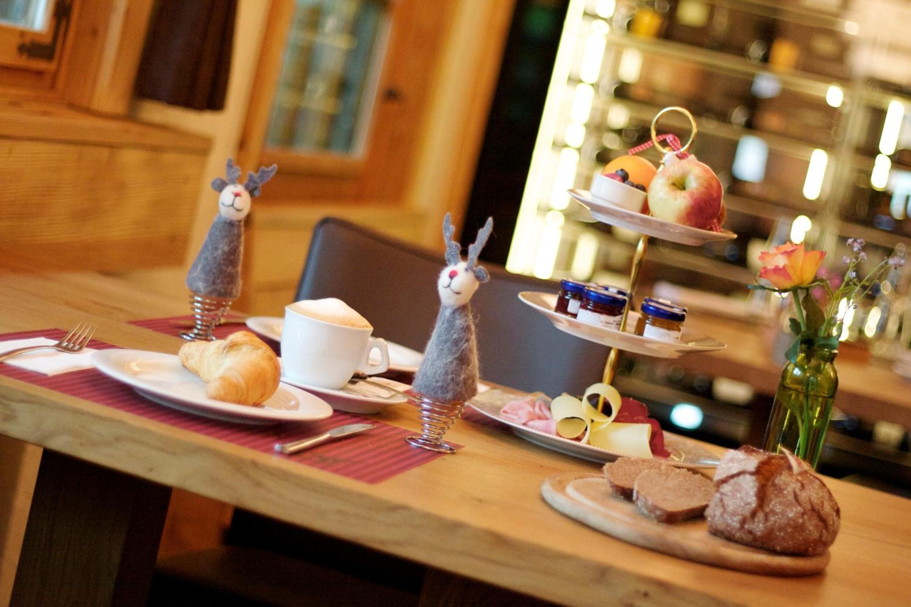 A dining table with croissants, a bowl of soup, and a tiered dessert stand with fruits and pastries.
