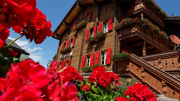 Un edificio tradizionale in legno con persiane rosse e balconi adornati da fioriere.
