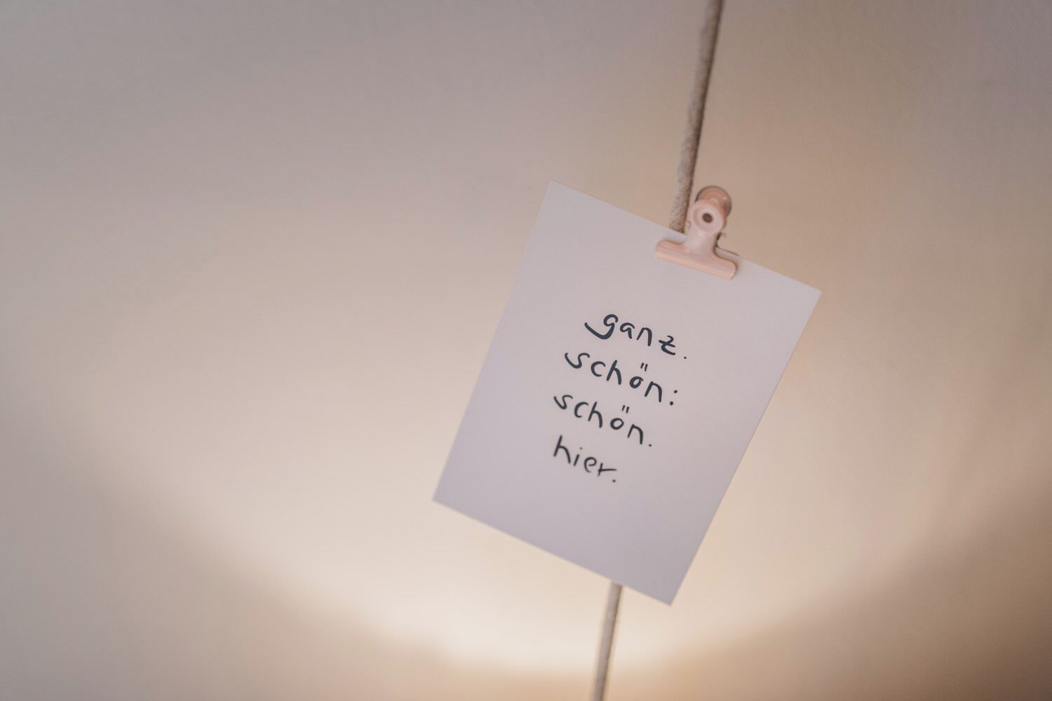 A note with text on a wall, clipped by a wooden clip.