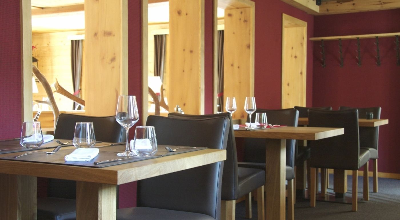 A restaurant with wooden tables and chairs, some with empty wine glasses and cutlery.