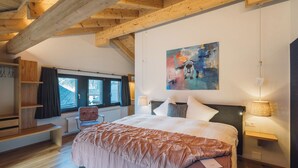 Una camera da letto con un letto grande, travi in legno, una finestra, una sedia e un quadro appeso al muro.