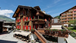 Un edificio tradizionale in legno con persiane rosse, un balcone fiorito e una scala che conduce a un piano superiore.