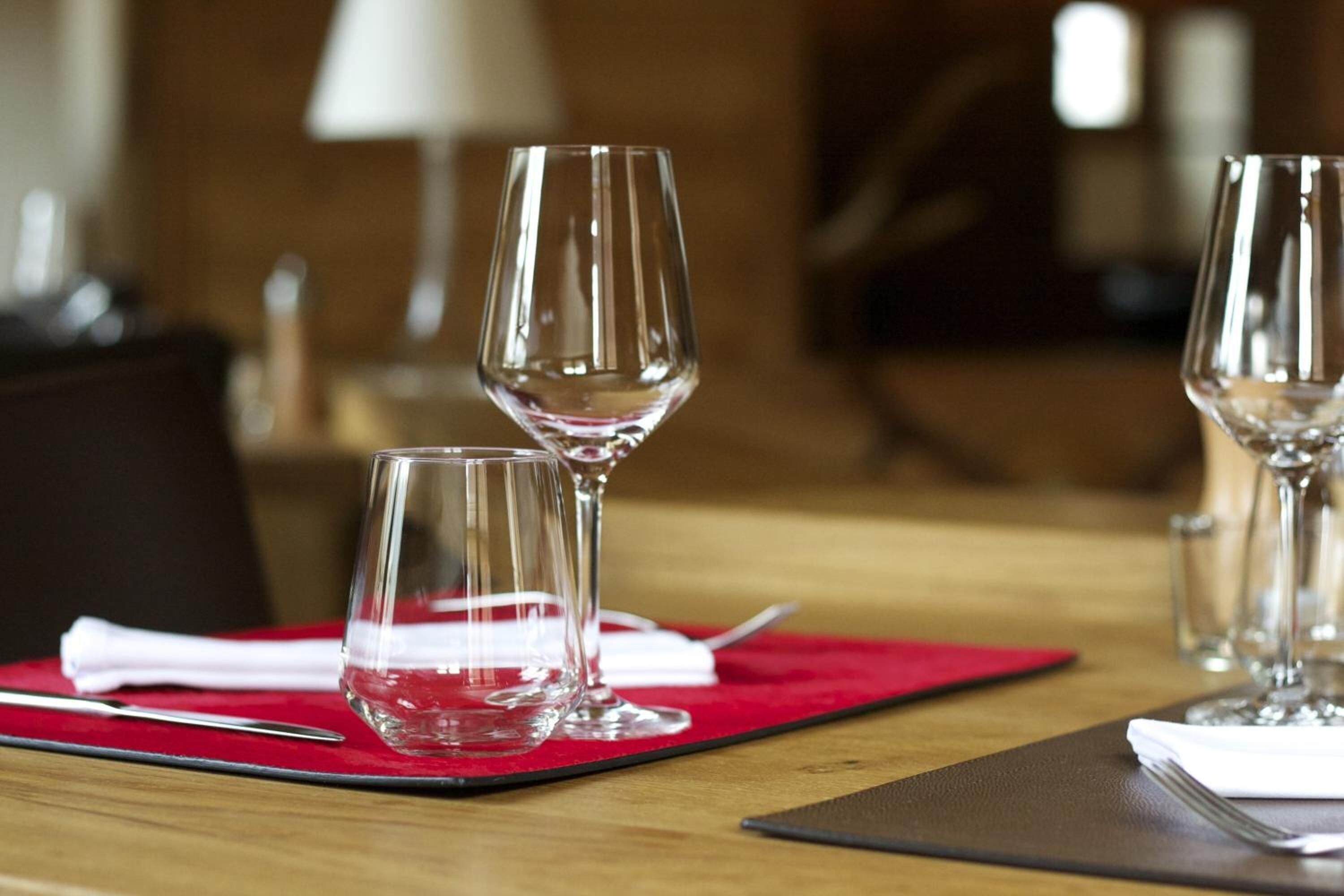 Una mesa de comedor con tres copas de vino y un tenedor sobre un mantel individual rojo.